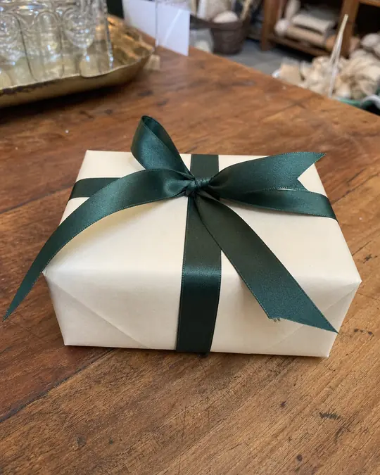 A phone photo of a cream gift box tied with a dark green ribbon on a wooden shop counter